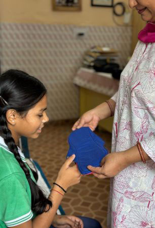 A woman giving a reusable cotton pad to a young girl.
