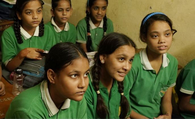 A group of schoolgirls in green uniforms listening attentively.